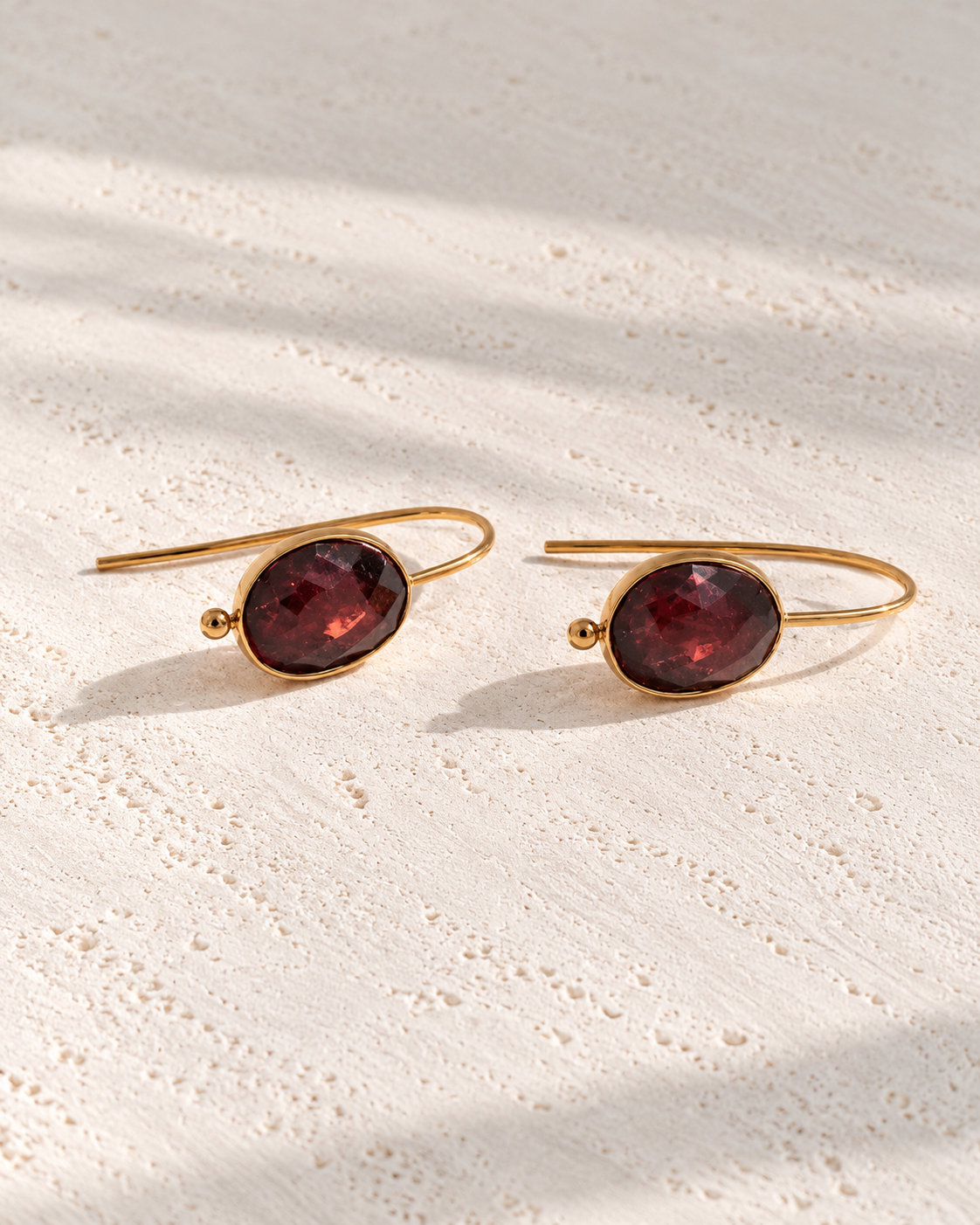 Pendientes Fiorella con piedra granate sobre cemento blanco